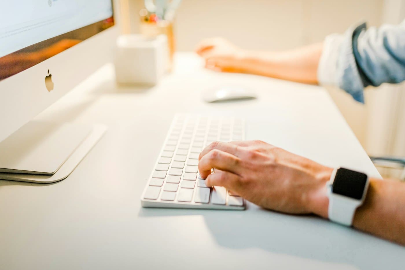 Hands typing on a keyboard at a bright desk